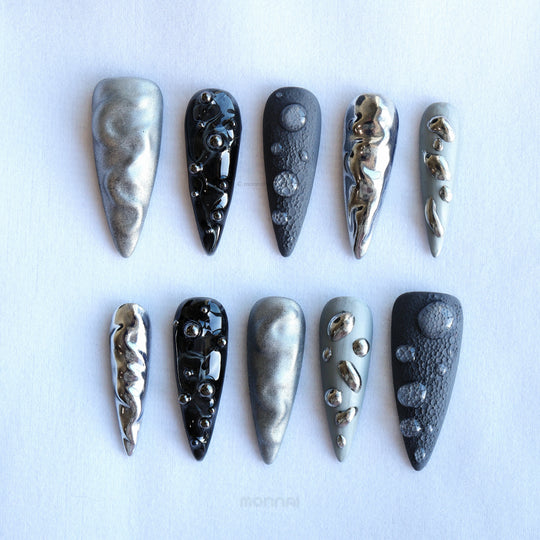 Dark Moon press-on nails laid out in silver, charcoal and black with crater texture and raised gel droplets