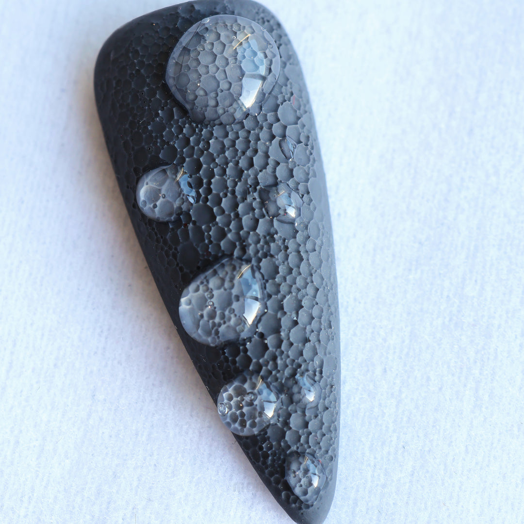 Dark Moon press-on nails in close-up, black sculptural nail with crater-like texture and raised gel droplets