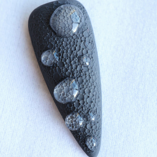 Dark Moon press-on nails in close-up, black sculptural nail with crater-like texture and raised gel droplets