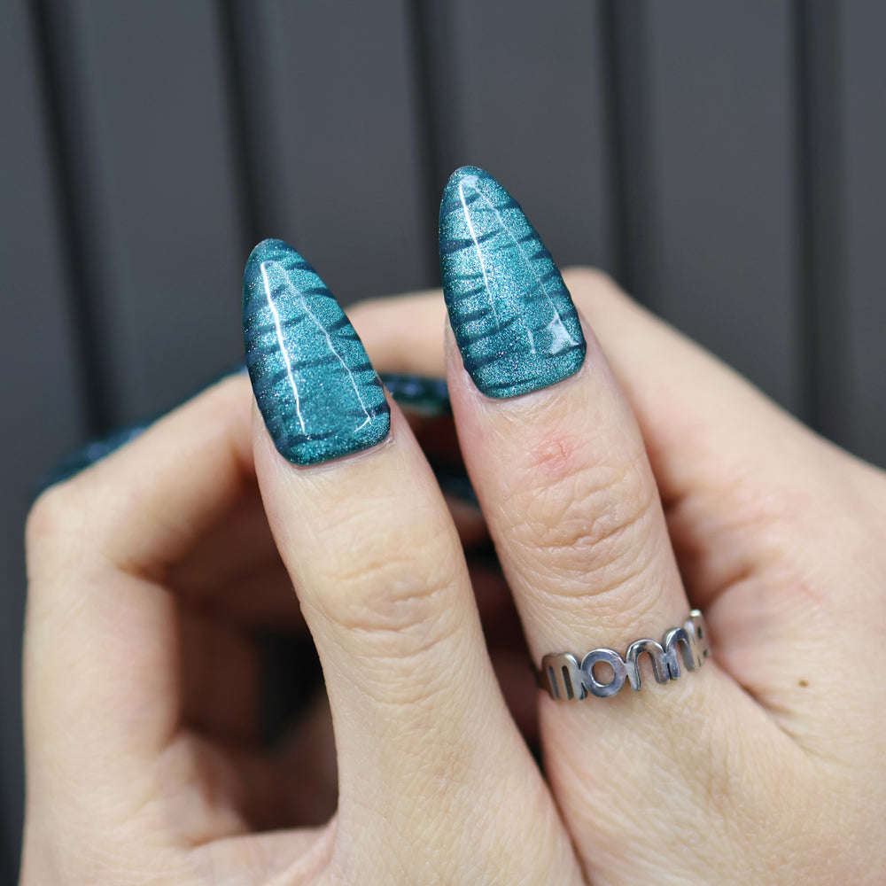 Deep Sea press-on nails on hand, teal cat-eye finish with raised zebra texture and glossy shine.