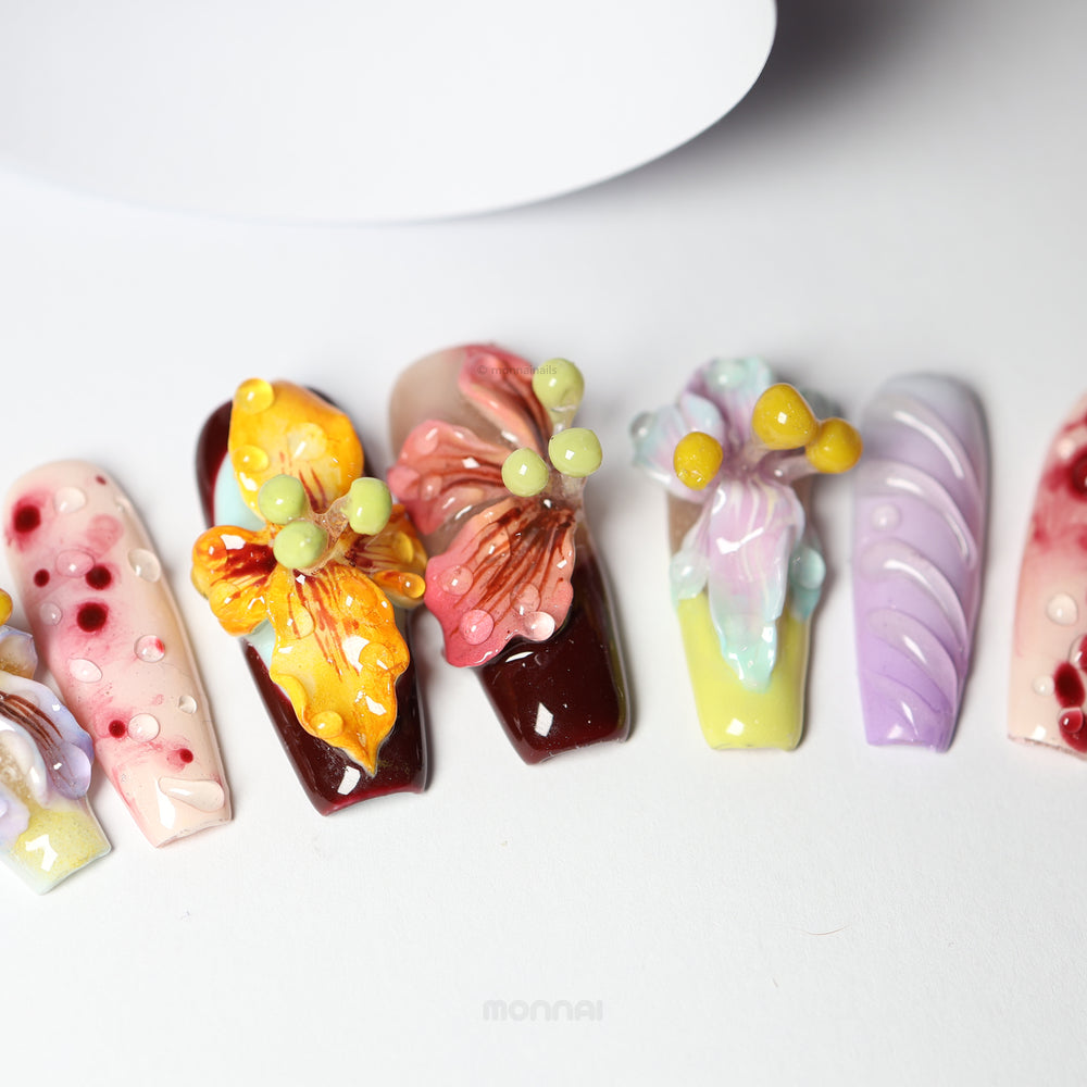 Dreamscape Blossoms press-on nails laid out in close-up, with hand-painted botanical blooms and glossy 3D dewdrops.