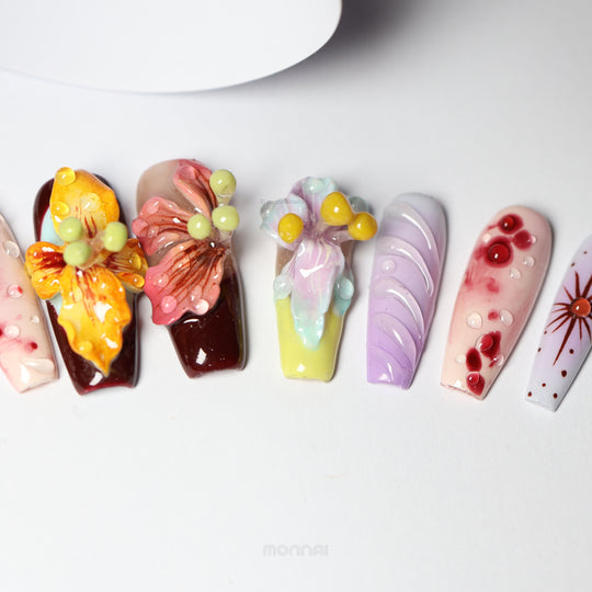 Dreamscape Blossoms press-on nails laid out in close-up, showing botanical 3D petals, dewdrops, and rich ochre, bordeaux, and lavender.