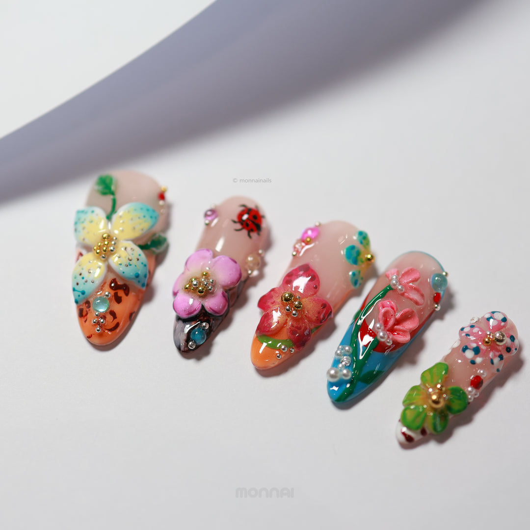 Enchanted Garden press-on nails laid out with 3D hand-painted flowers, butterfly accents, and colorful botanical details.