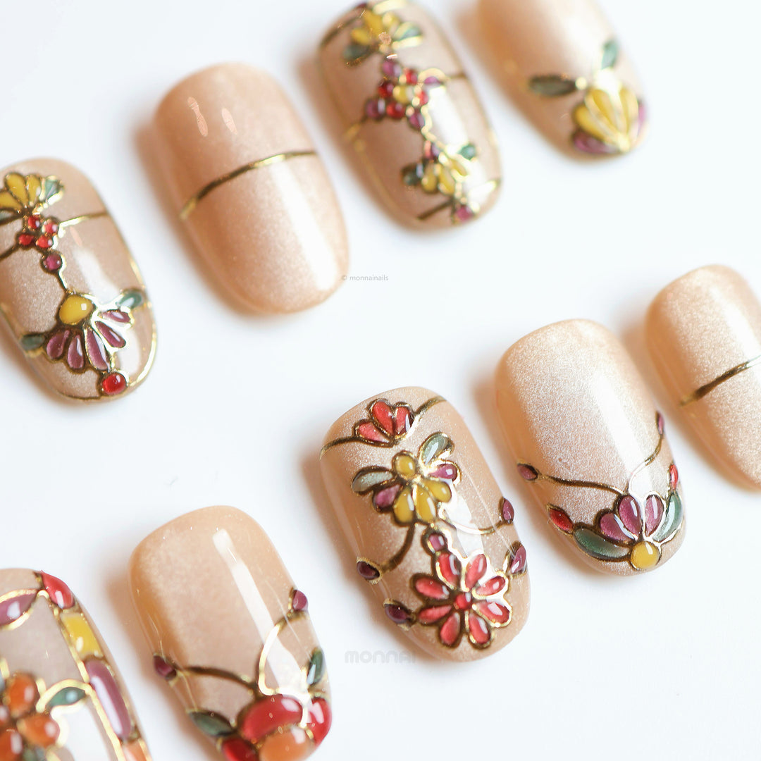 Eternal Grace press-on nails laid out, showing champagne-gold shimmer with vintage stained-glass florals and metallic linework.