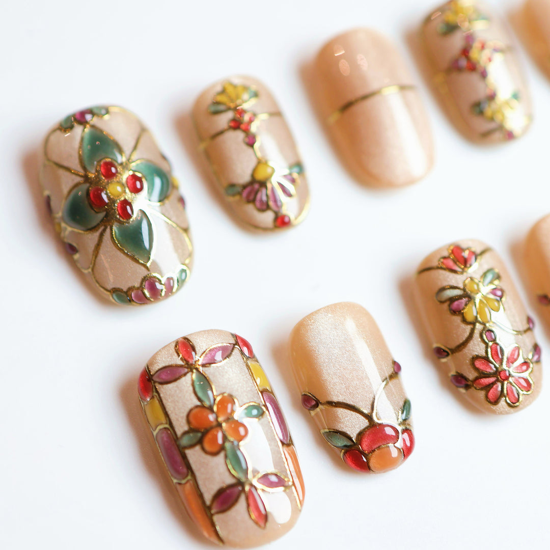 Eternal Grace press-on nails laid out, champagne-gold stained-glass florals with gold linework and jewel accents