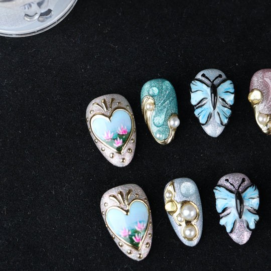 Ethereal Reverie press-on nails laid out, featuring butterfly and floral details, pearl accents, and sculpted frames.