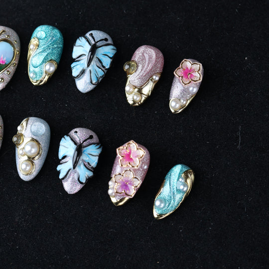 Ethereal Reverie press-on nails laid out in close-up, showing butterfly, floral, pearl, and gold-framed shimmer details.