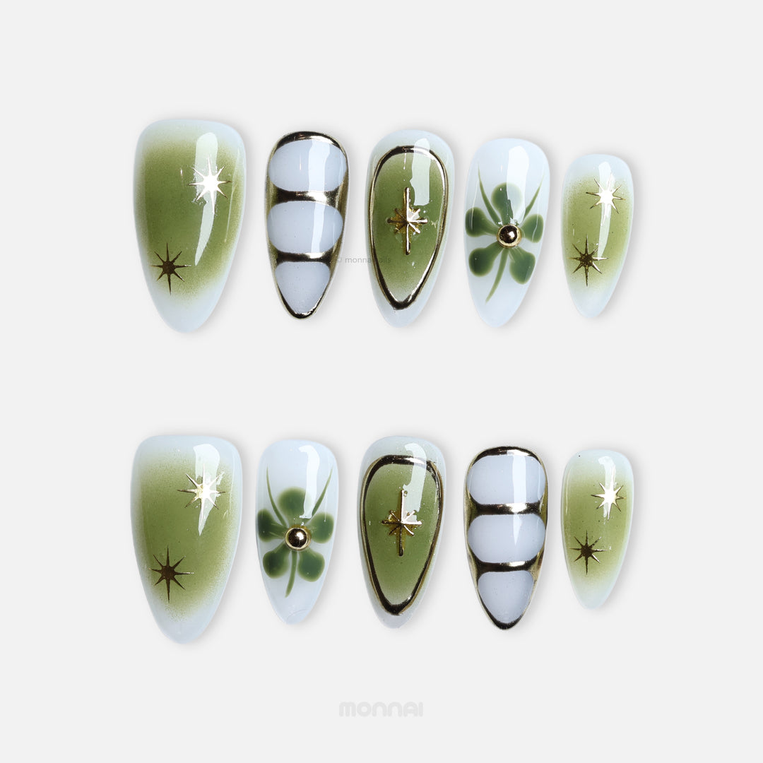 Evergreen press-on nails laid out with green gradients, clover-like florals, fine linework and gold star accents