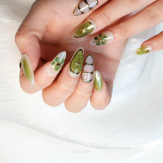 Evergreen press-on nails worn on hand, soft green gradients with gold star accents and clover-like florals