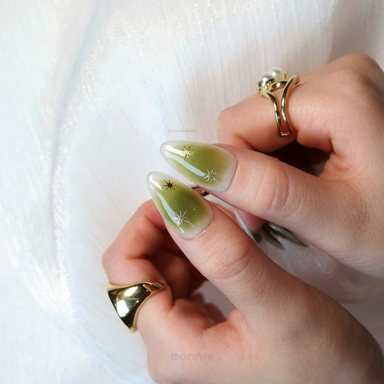 Evergreen press-on nails on hand, soft green gradient with gold star accents and minimal sheer finish