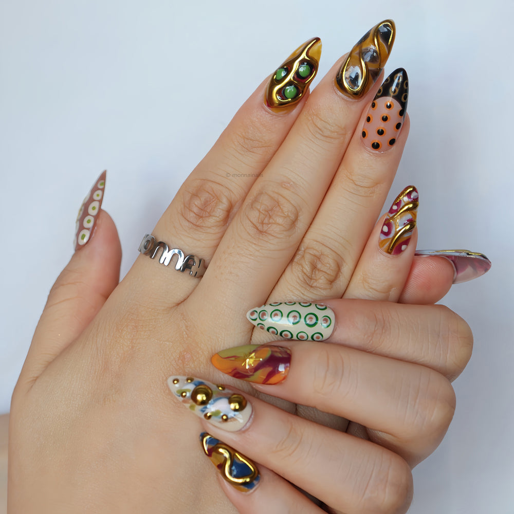 Everything Everywhere in Gold press-on nails on hands, with gold chrome accents, abstract swirls, and retro dots in an artsy, bold style.
