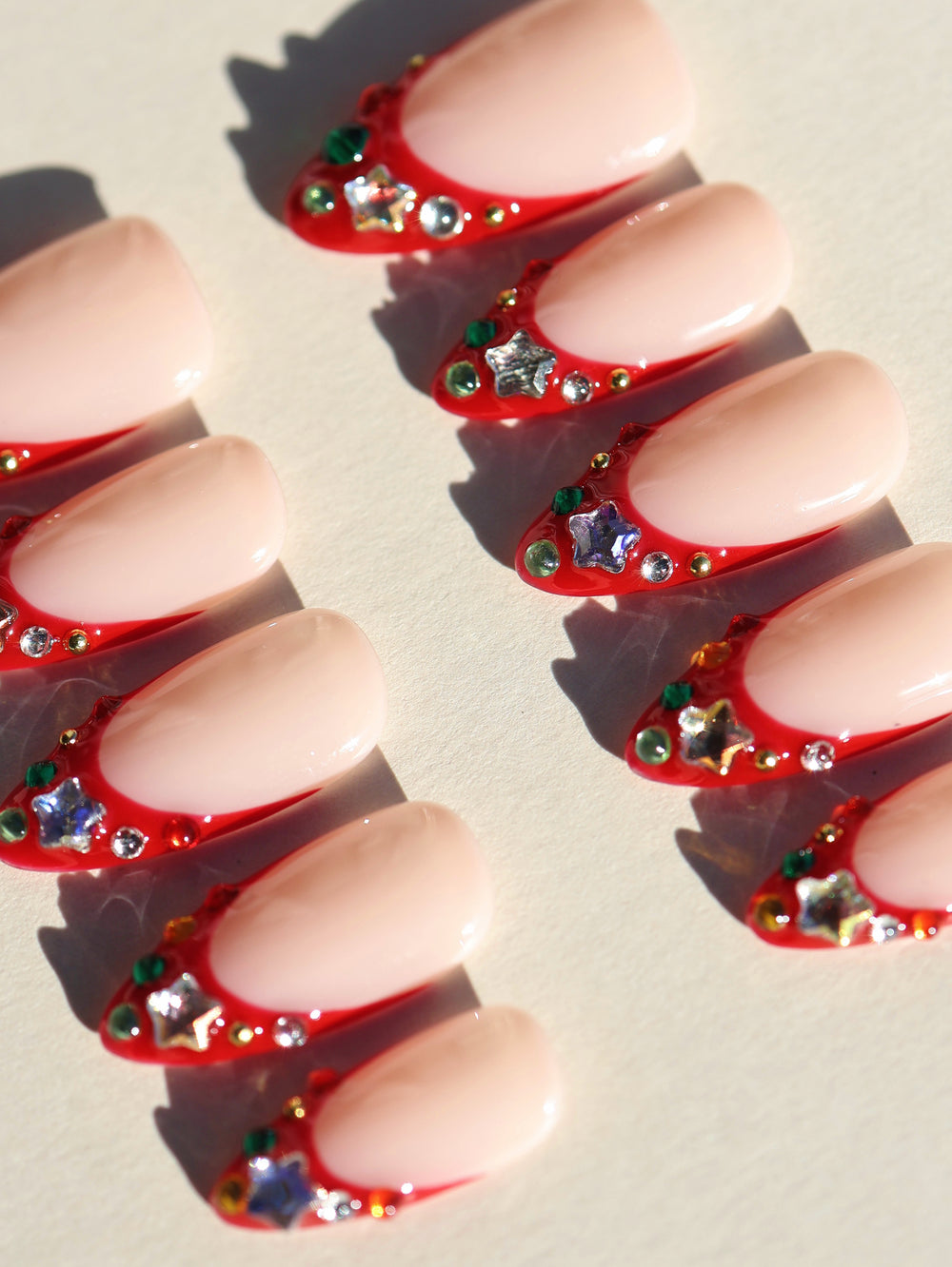 Festive Jewels press-on nails laid out in rows with nude bases, red French tips, and crystal star accents