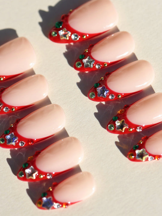 Festive Jewels press-on nails laid out in rows with nude bases, red French tips, and crystal star accents