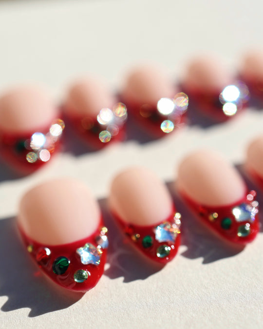 Festive Jewels press-on nails with red French tips and crystal stars laid out in close-up
