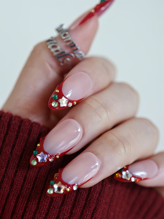 Festive Jewels press-on nails on hand with red French tips, crystal stars, colorful jewels, and a glossy nude base.