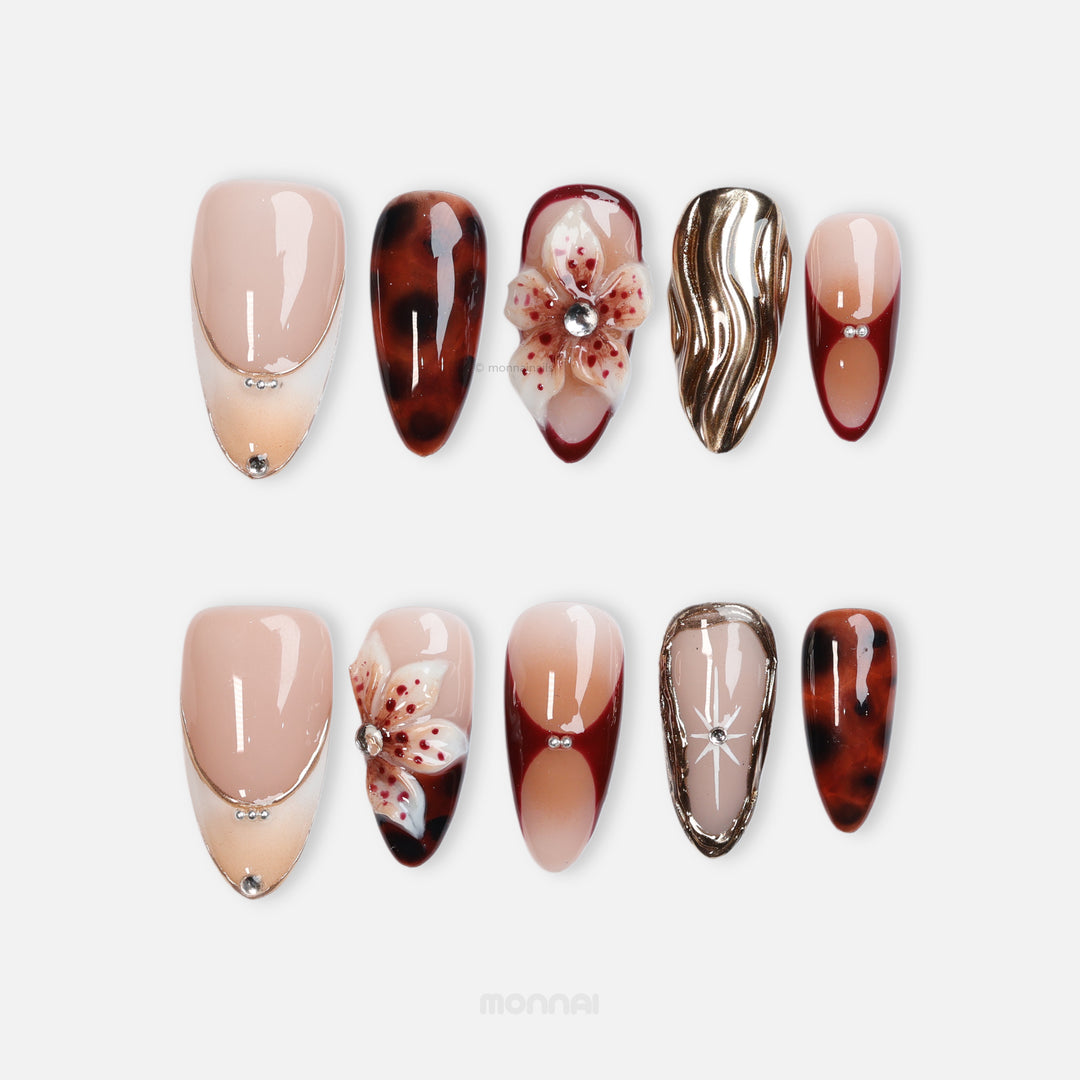 Flame Fleur press-on nails shown laid out, with nude bases, tortoiseshell, burgundy French details, floral accents and gold texture.