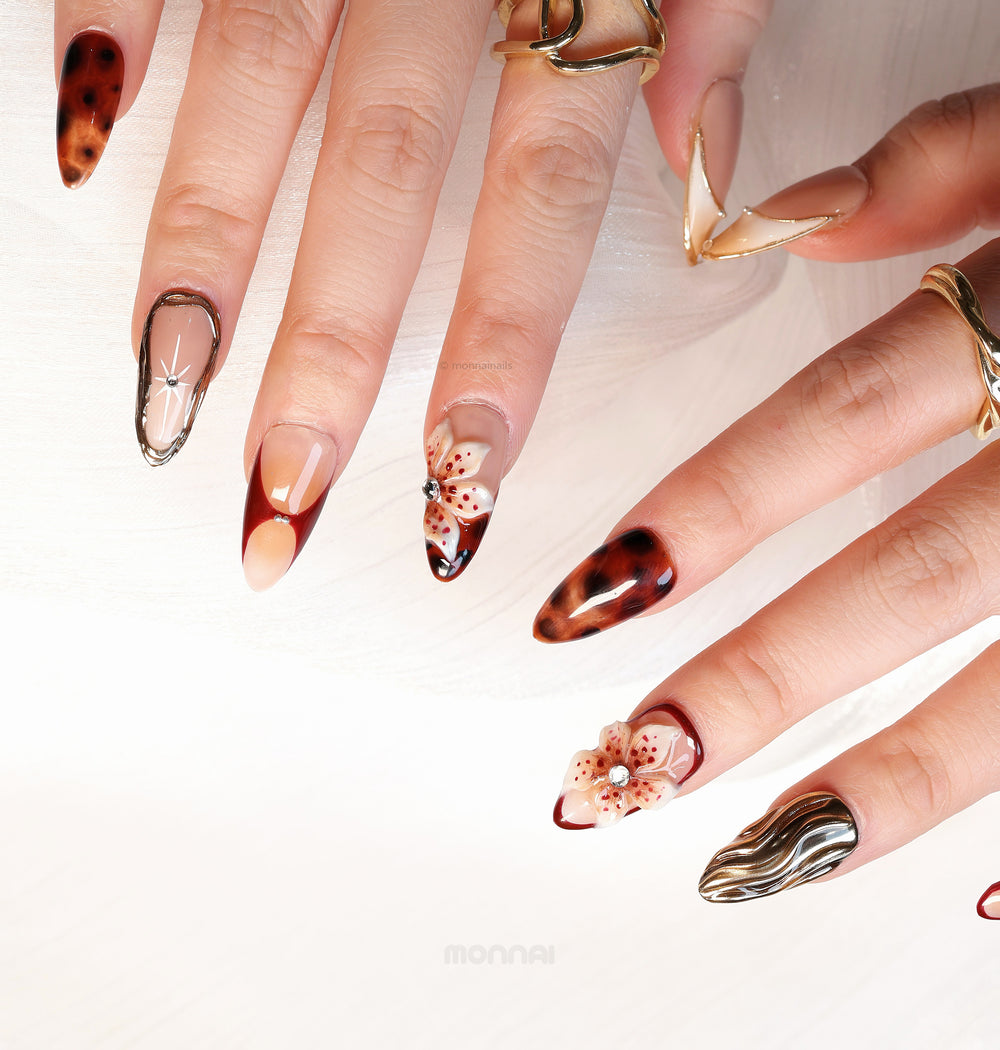 Flame Fleur press-on nails with autumn tones, tortoiseshell, burgundy French tips, floral accents, and gold texture on hands