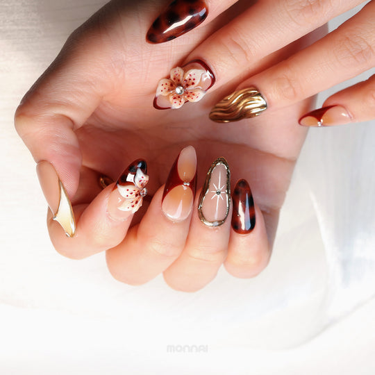 Flame Fleur press-on nails worn on hand, with autumnal burgundy, tortoiseshell, floral accents, and gold texture.