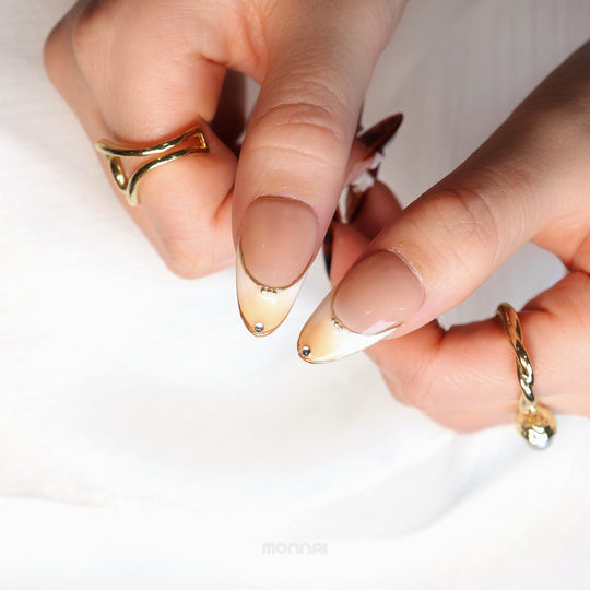 Flame Fleur press-on nails in close-up, nude almond tips with gold outlines and tiny silver accents