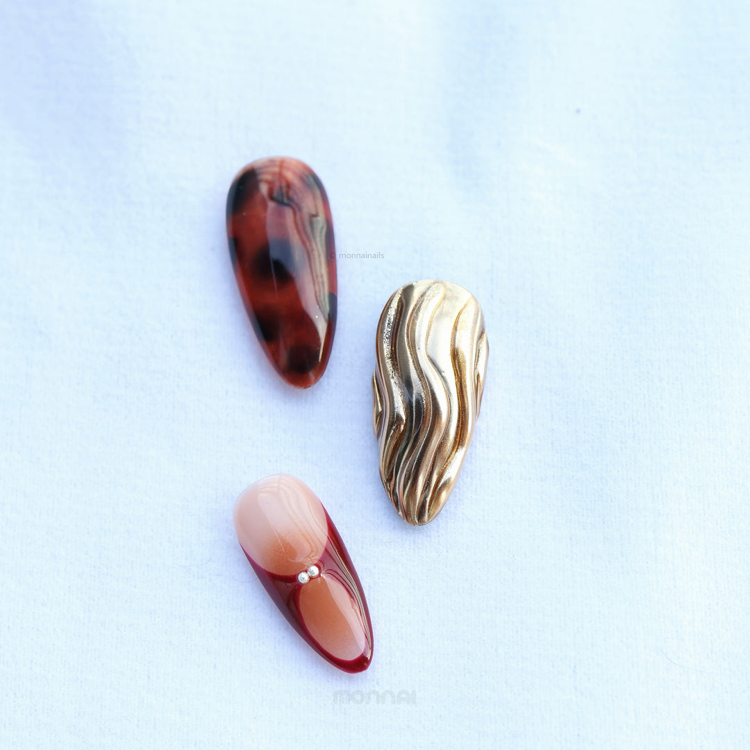 Flame Fleur press-on nails laid out with tortoiseshell, burgundy French tips, nude and molten gold texture