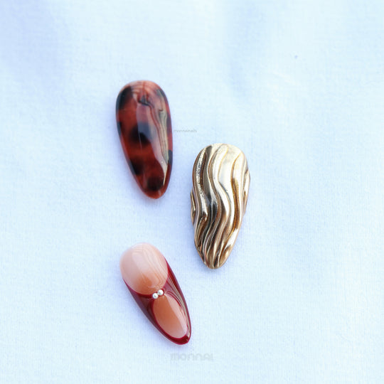 Flame Fleur press-on nails laid out with tortoiseshell, burgundy French tips, nude and molten gold texture