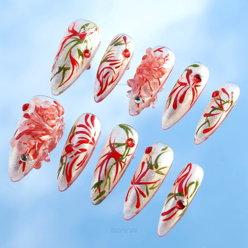 Flame Rebirth press-on nails laid out, showing silver cat-eye shine with red floral strokes and green accents.