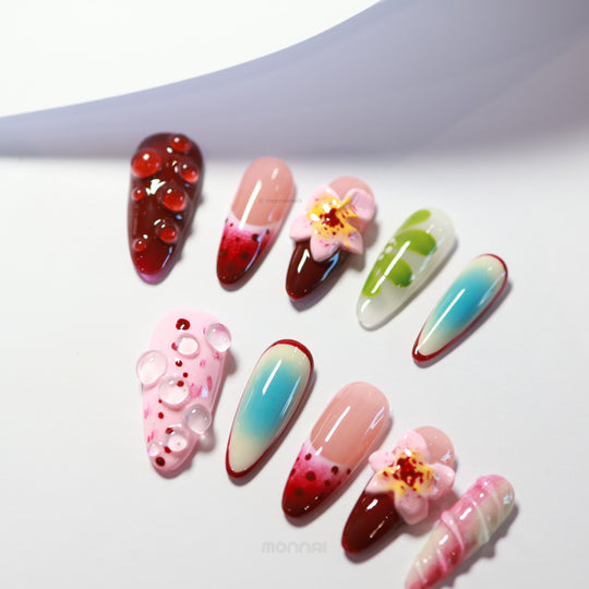 Floral Bliss press-on nails laid out, featuring rich cherry red, pastel pink, sky-blue aura gradients, hand-painted florals, and clear dewdrops.