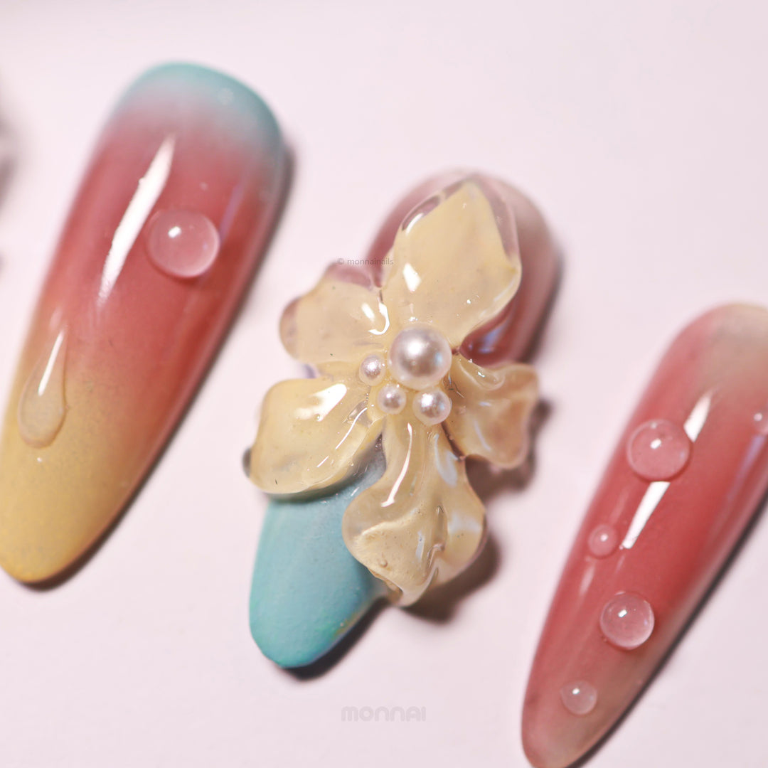 Floral Sunset press-on nails in close-up, with glossy gradient nails and a sculpted 3D flower accented by bubble-like droplets.