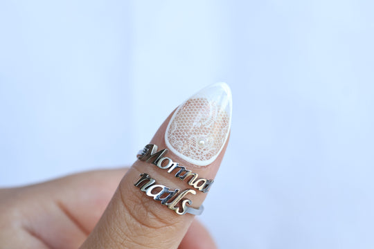Floral Veil press-on nails shown on a thumb, sheer white floral lace with a micro pearl accent and glossy finish.