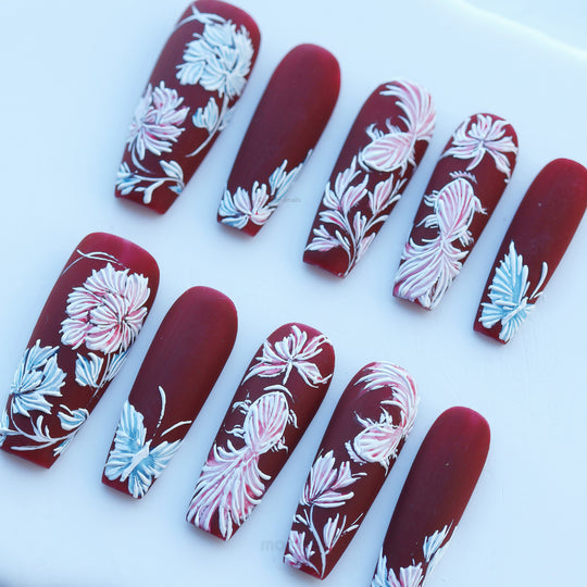 Flutter &amp; Flow press-on nails in deep burgundy matte with hand-painted floral embroidery-style details, laid out in close-up