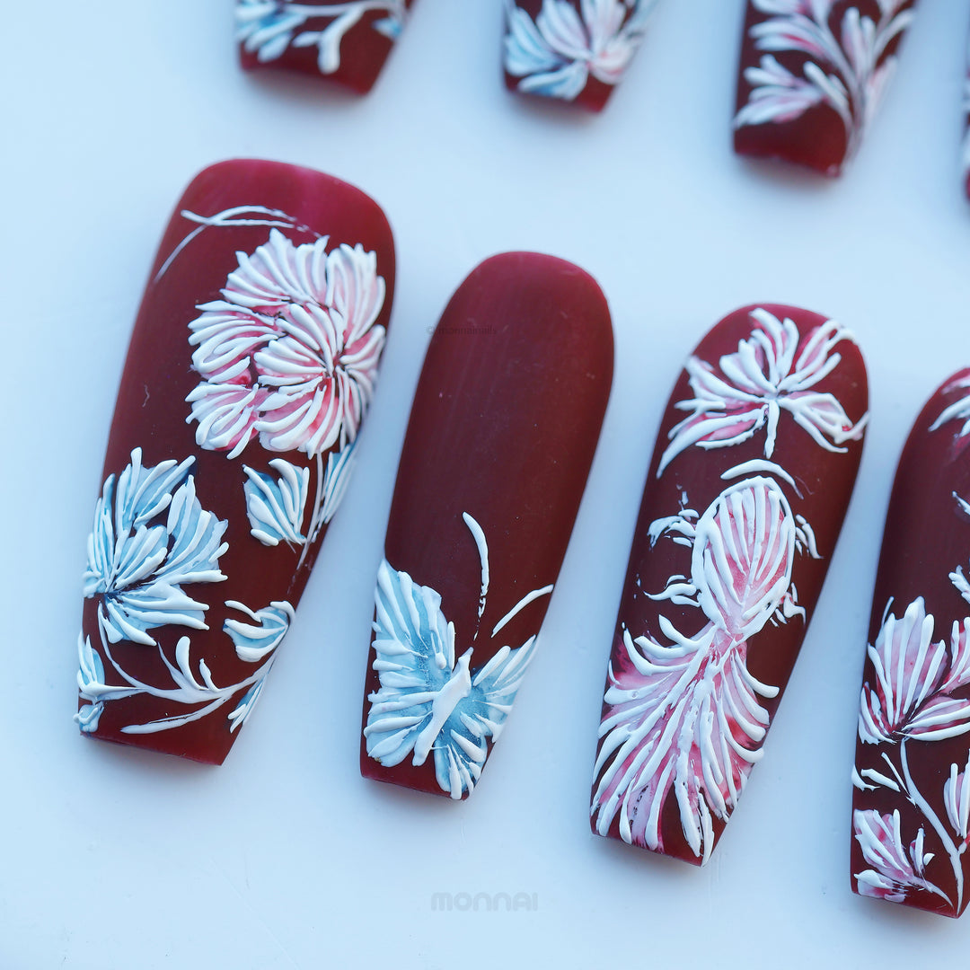 Flutter &amp; Flow press-on nails shown laid out, deep red matte with hand-painted floral embroidery-style details in a vintage feel.