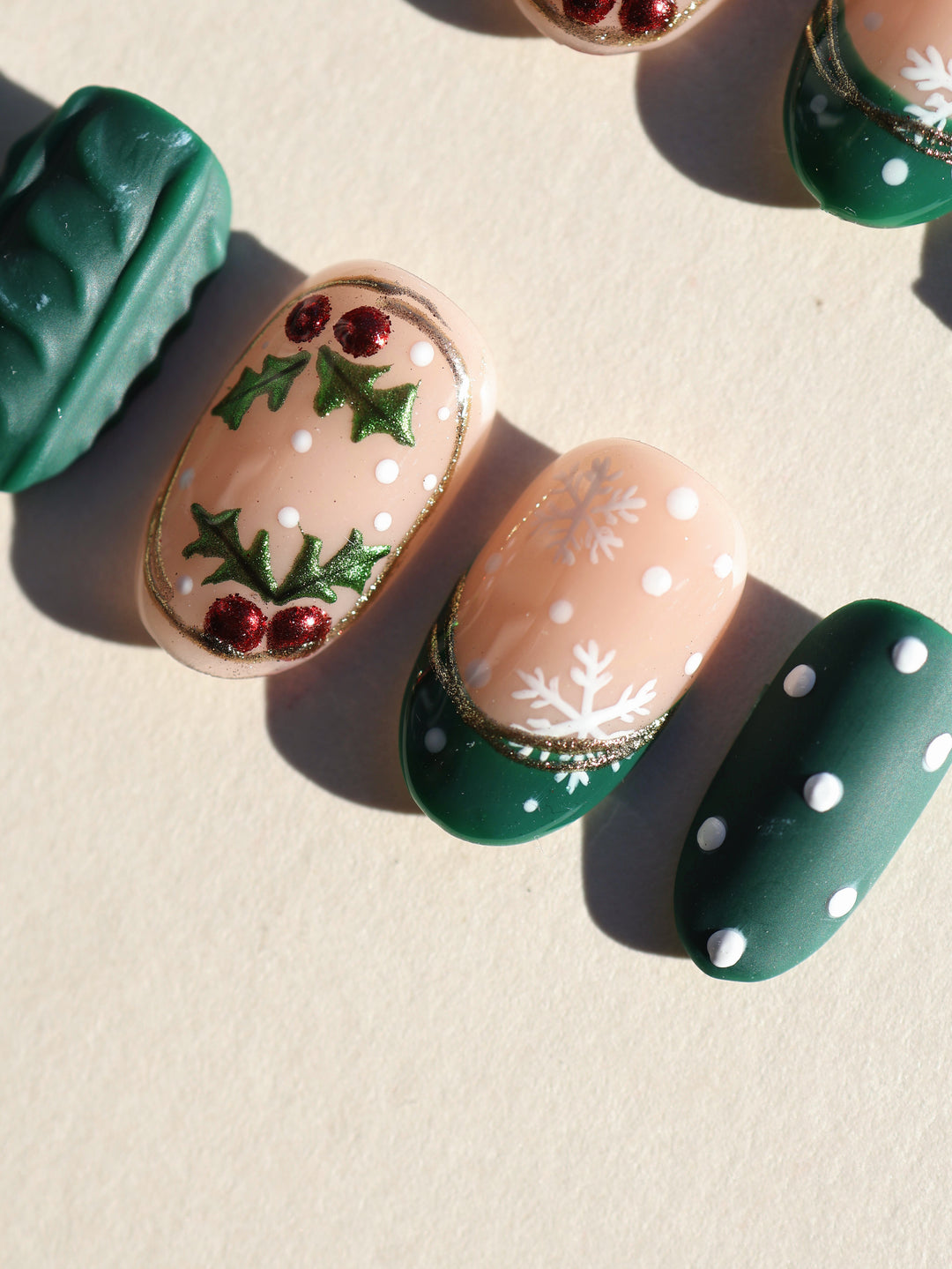 Forest Dots press-on nails close-up: nude almond nails with green holly, white snowflakes, red berries and white dots