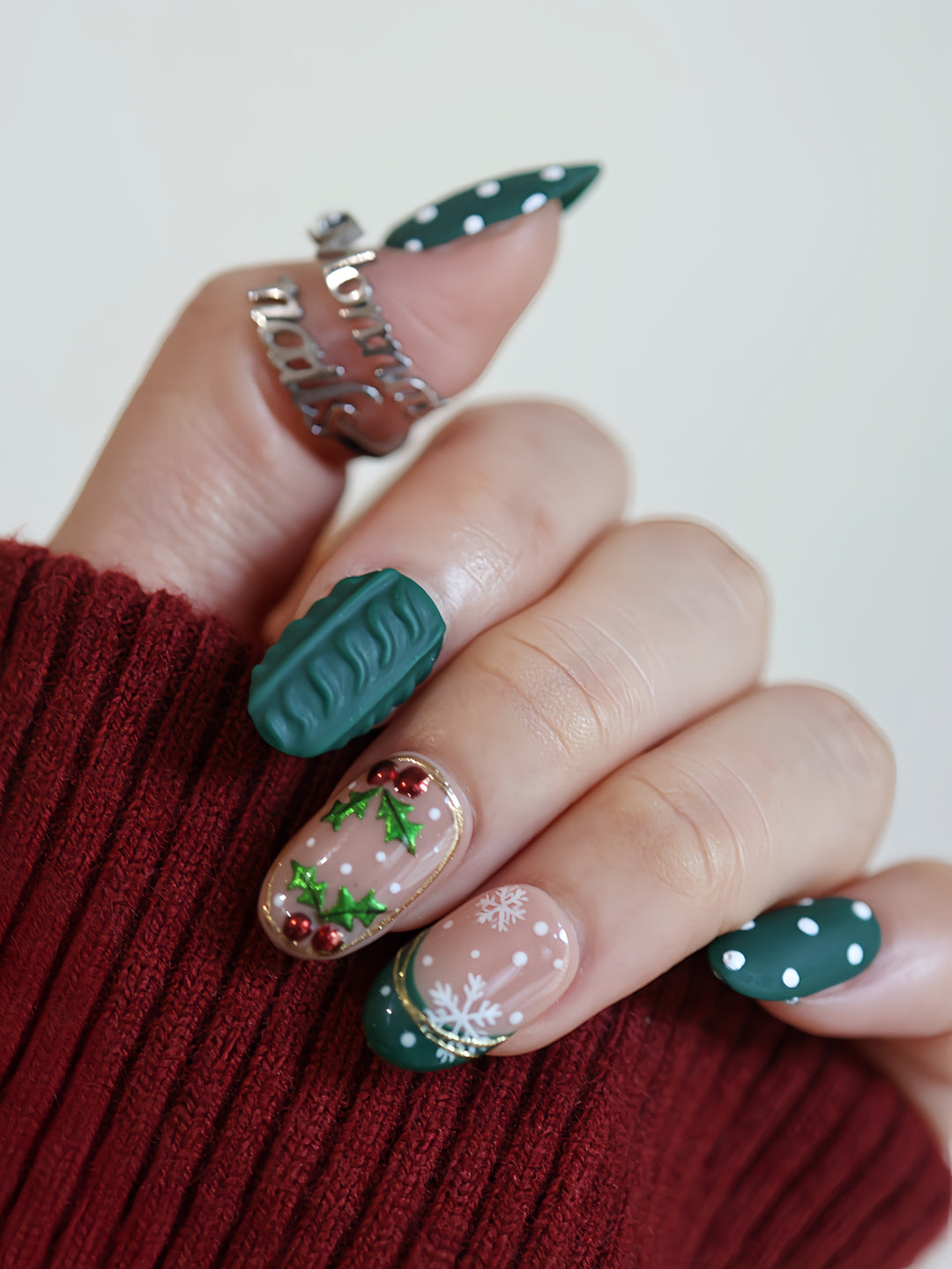 Forest Dots press-on nails worn on hand, green and nude oval nails with polka dots, knit texture and festive holly details