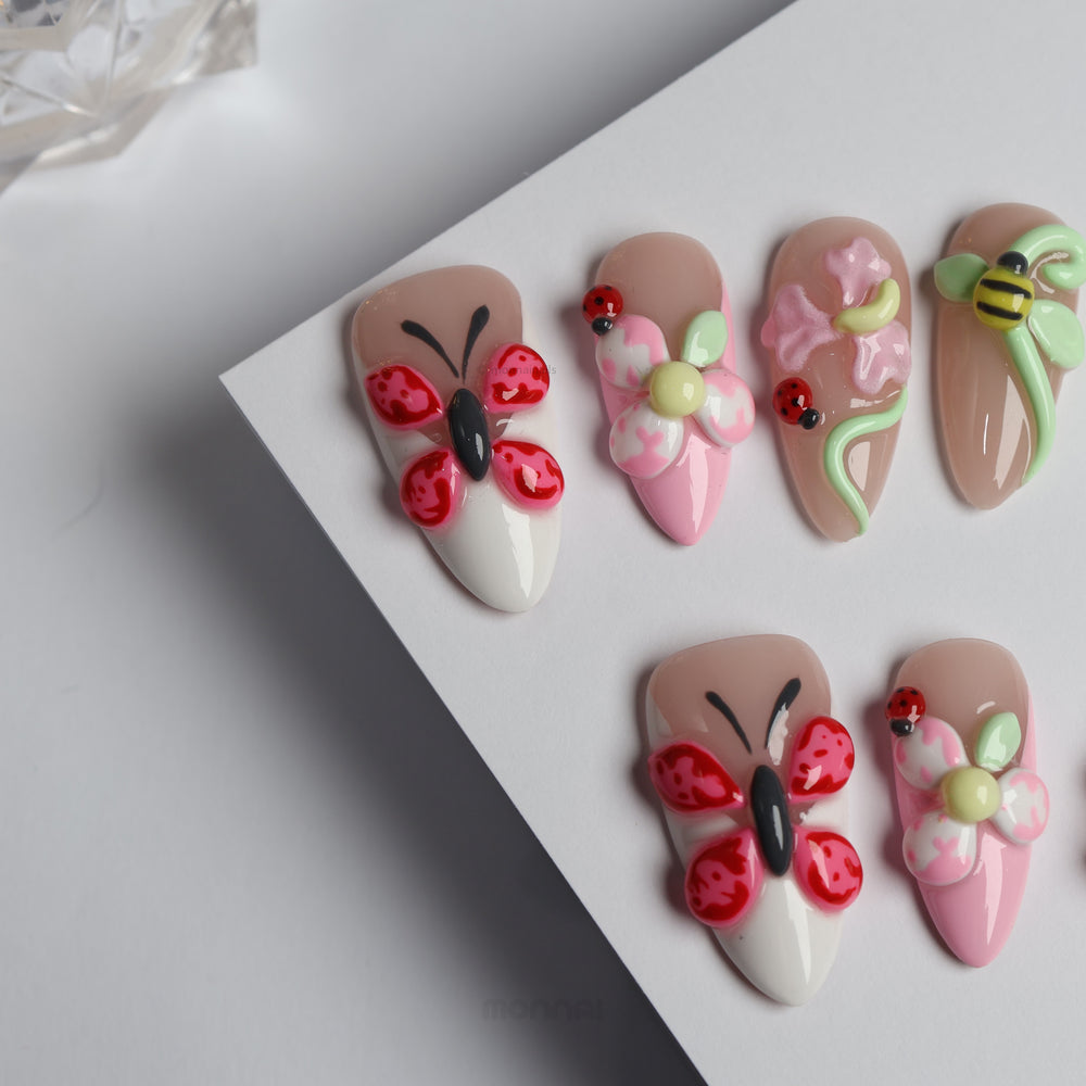 Garden Party press-on nails laid out in close-up, with glossy butterfly, blossom, ladybug and bee details in nude, pink and white.