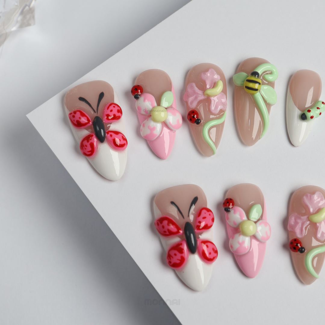 Garden Party press-on nails laid out with glossy nude, white and pink floral details, butterflies, ladybugs and a bee
