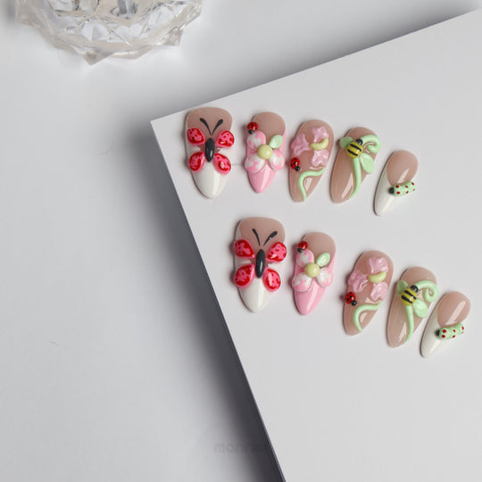 Garden Party press-on nails laid out with butterfly, blossom, ladybug and bee 3D accents in soft nude and milky white tones.