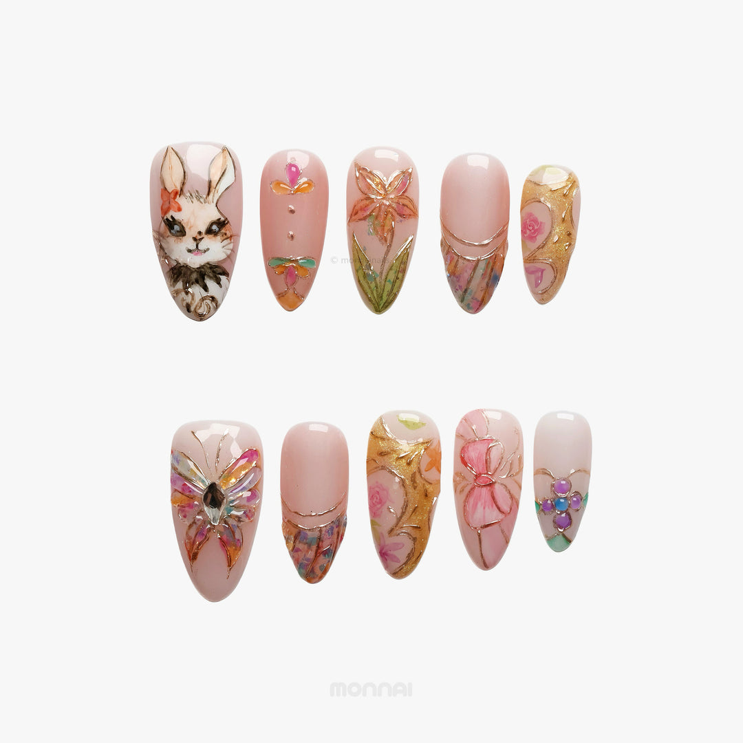 Garden Tales press-on nails laid out with blush pink glass-like floral designs, a bunny, and gold accents