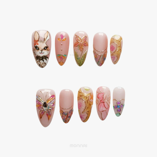 Garden Tales press-on nails laid out with blush pink glass-like floral designs, a bunny, and gold accents
