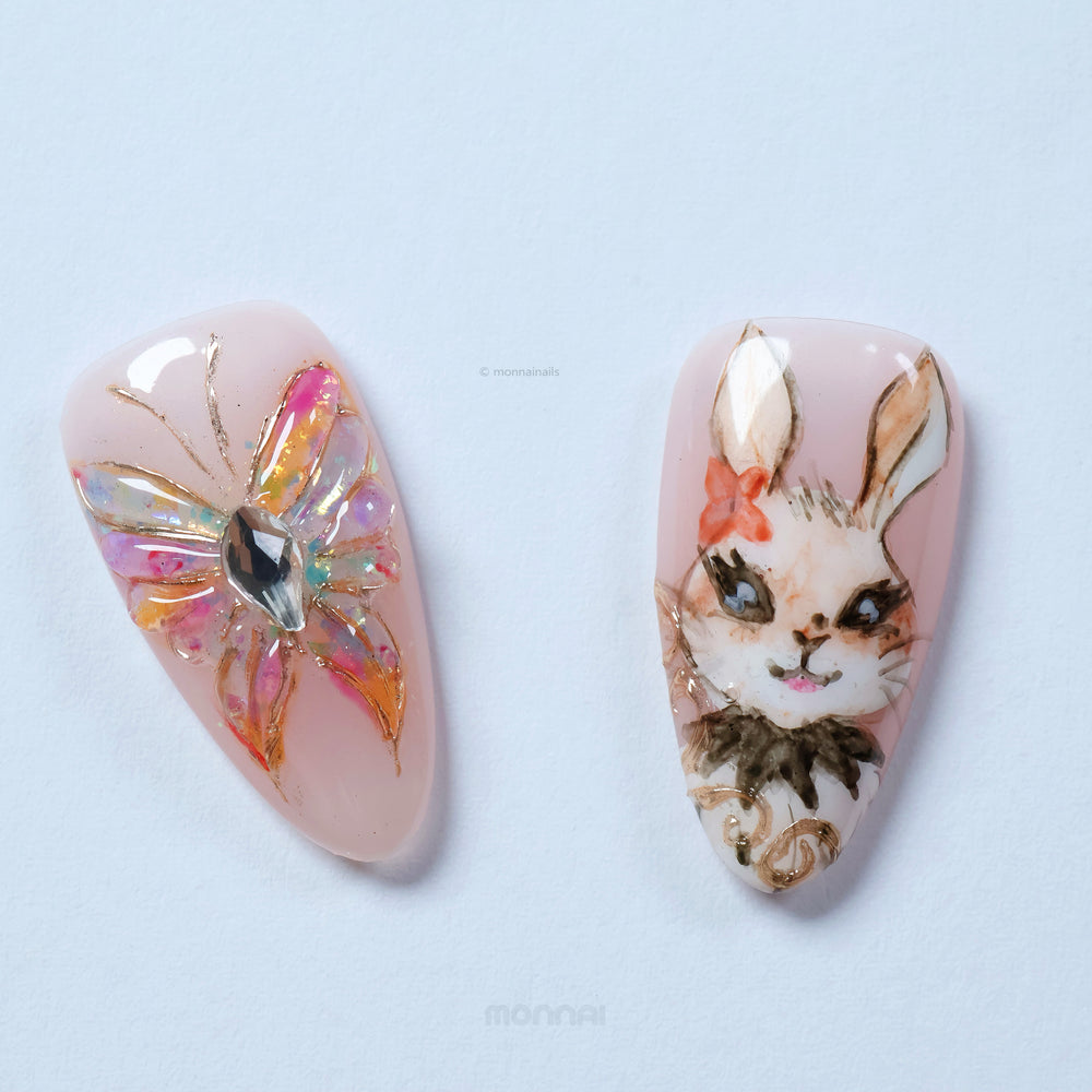 Garden Tales press-on nails laid out in close-up, with blush pink floral art, a bunny face and gold accents.