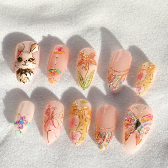 Garden Tales press-on nails laid out, featuring blush pink whimsical floral designs, a bunny accent, and gold details.