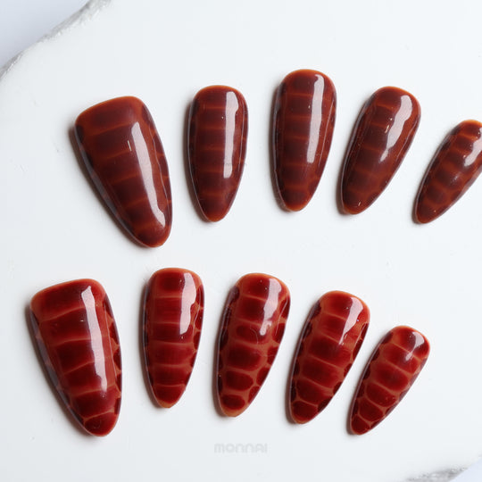Gator Glaze press-on nails in deep brown with glossy crocodile texture, shown laid out in close-up