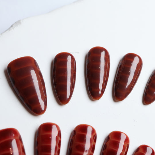 Gator Glaze press-on nails in deep brown with subtle crocodile texture, shown laid out in close-up
