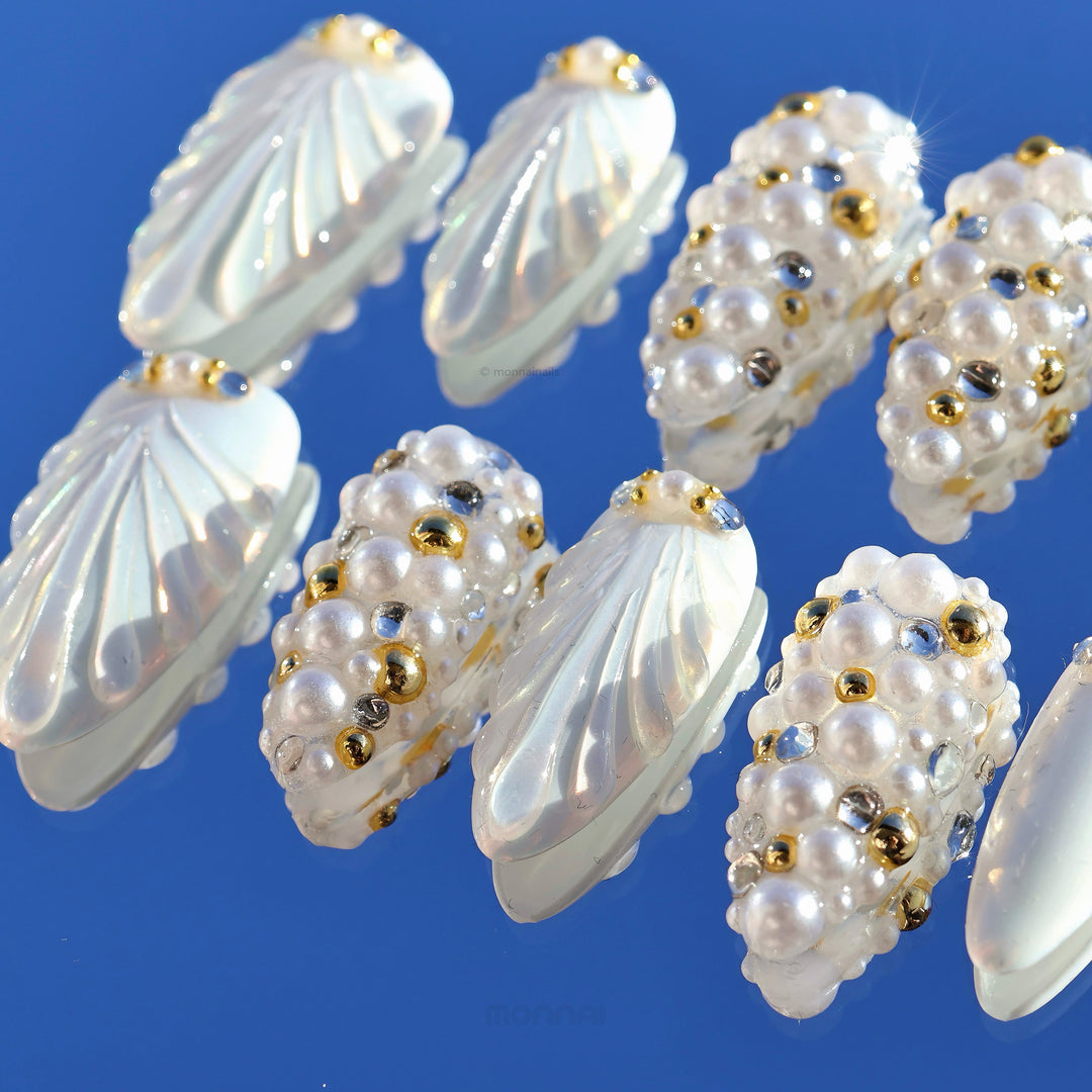 Gilded Pearls press-on nails laid out, showing milky shell textures with clustered pearls and crystal accents.