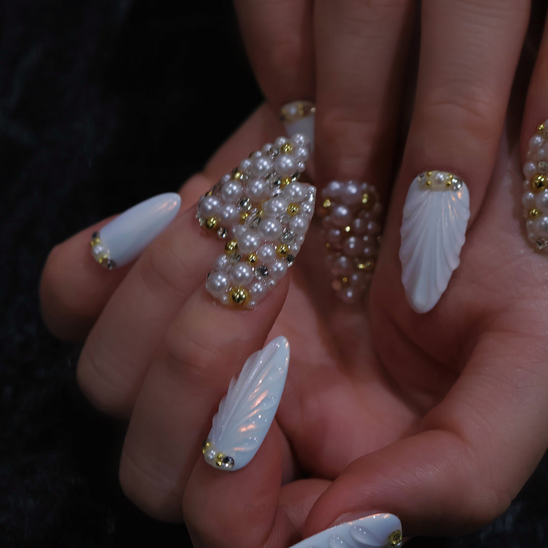 Gilded Pearls press-on nails on hand, showing milky white shell textures and clustered pearls with gold accents