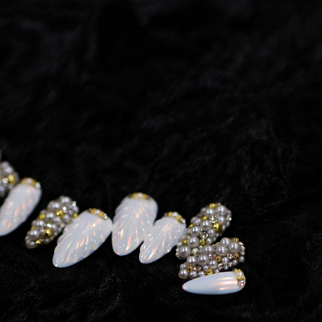 Gilded Pearls press-on nails laid out in close-up, with milky shell-like textures, clustered pearls, and crystal accents.