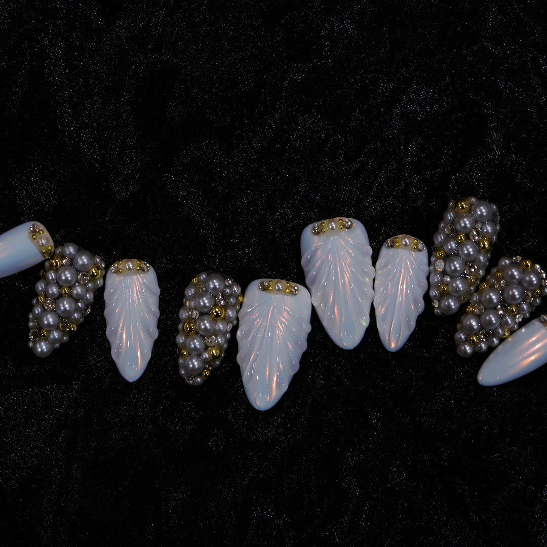 Gilded Pearls press-on nails laid out in close-up, showing milky shell textures and clustered pearls with gold accents.
