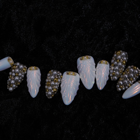 Gilded Pearls press-on nails laid out in close-up, showing milky shell textures and clustered pearls with gold accents.