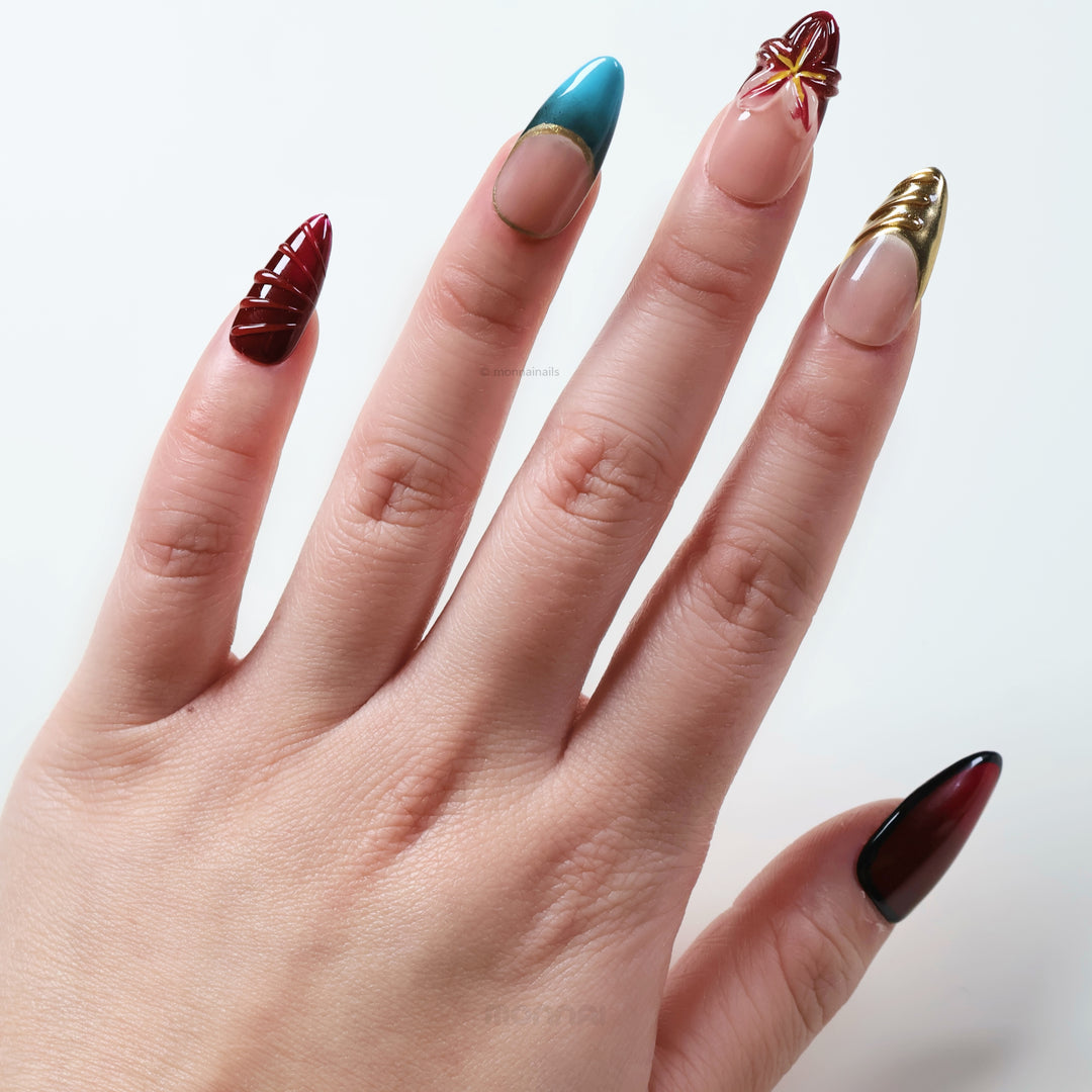 Gilded Rouge press-on nails shown on hand, with deep wine red, gold and nude sculpted floral details.
