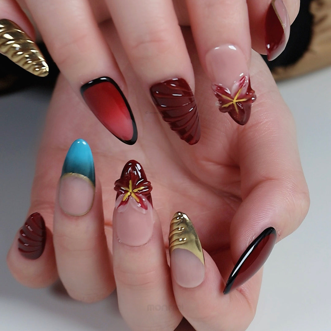 Gilded Rouge press-on nails worn on hand, showing wine red, nude, gold accents and sculpted floral details.