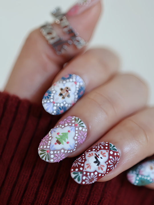 Ginger Cookie Christmas-themed press-on nails worn on hand, showing floral folk art, a tree, snowman, and gingerbread details.